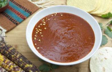 white-bowl-of-New-Mexican-style-red-chile-sauce-garnished-with-seeds-and-tortillas