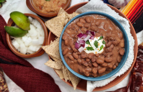 Trading-post-pinto-bean-dish-garnished-with-sour-cream-red-onions-and-cilantro-in-blue-bowl