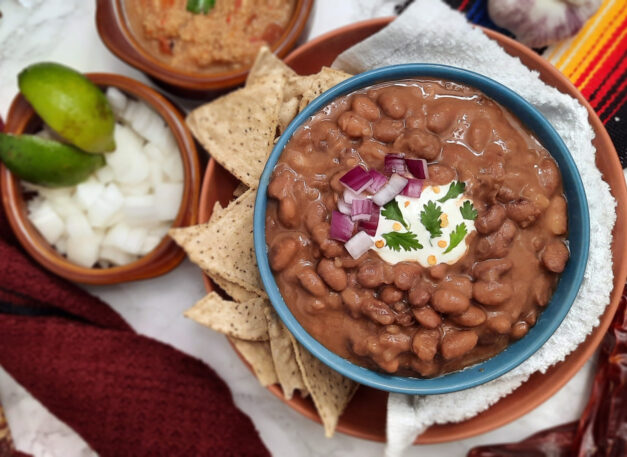 Trading-post-pinto-bean-dish-garnished-with-sour-cream-red-onions-and-cilantro-in-blue-bowl