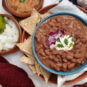 Trading-post-pinto-bean-dish-garnished-with-sour-cream-red-onions-and-cilantro-in-blue-bowl