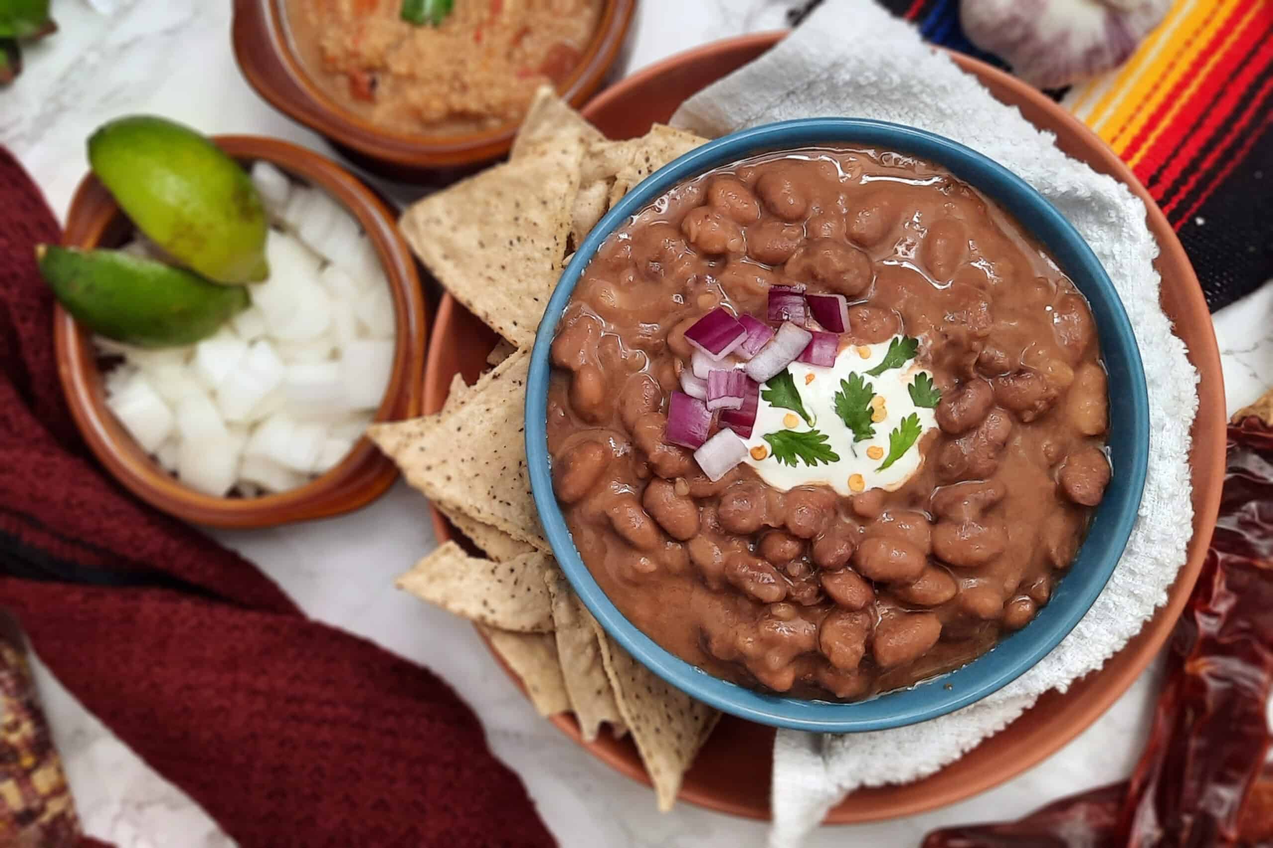 Trading-post-pinto-bean-dish-garnished-with-sour-cream-red-onions-and-cilantro-in-blue-bowl