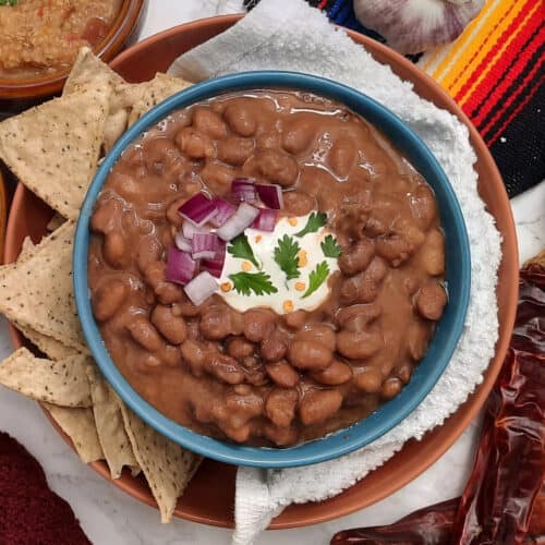 centered-bowl-of-Trading-Post-Beans-with-tortilla-chips-sour-cream-onions-and-cilantro-in-blue-bowl