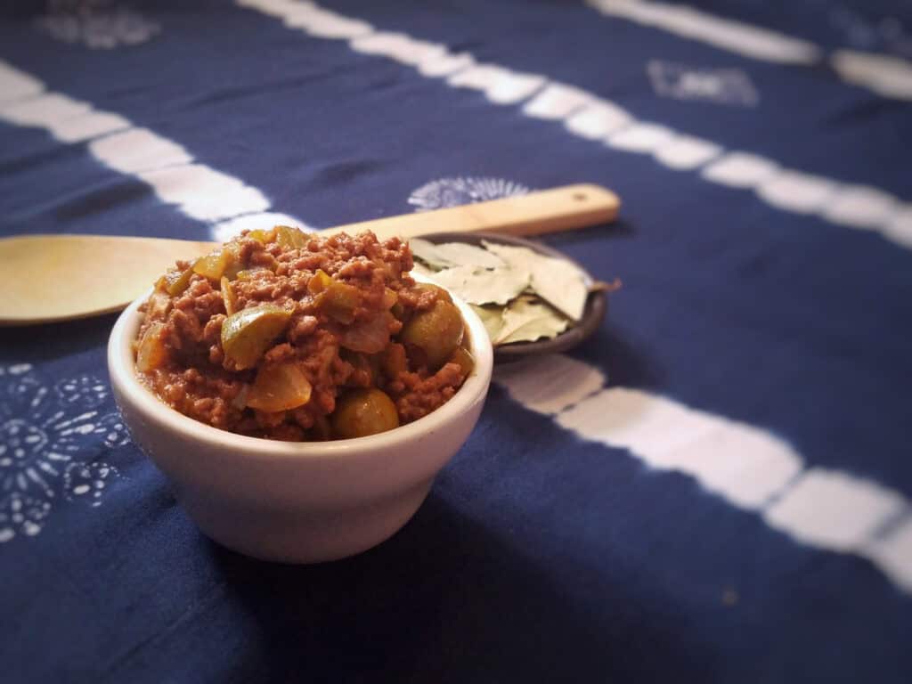 side-view-Cuban-picadillo-in-white-bowl-with-wooden-spoon-on-blue-background