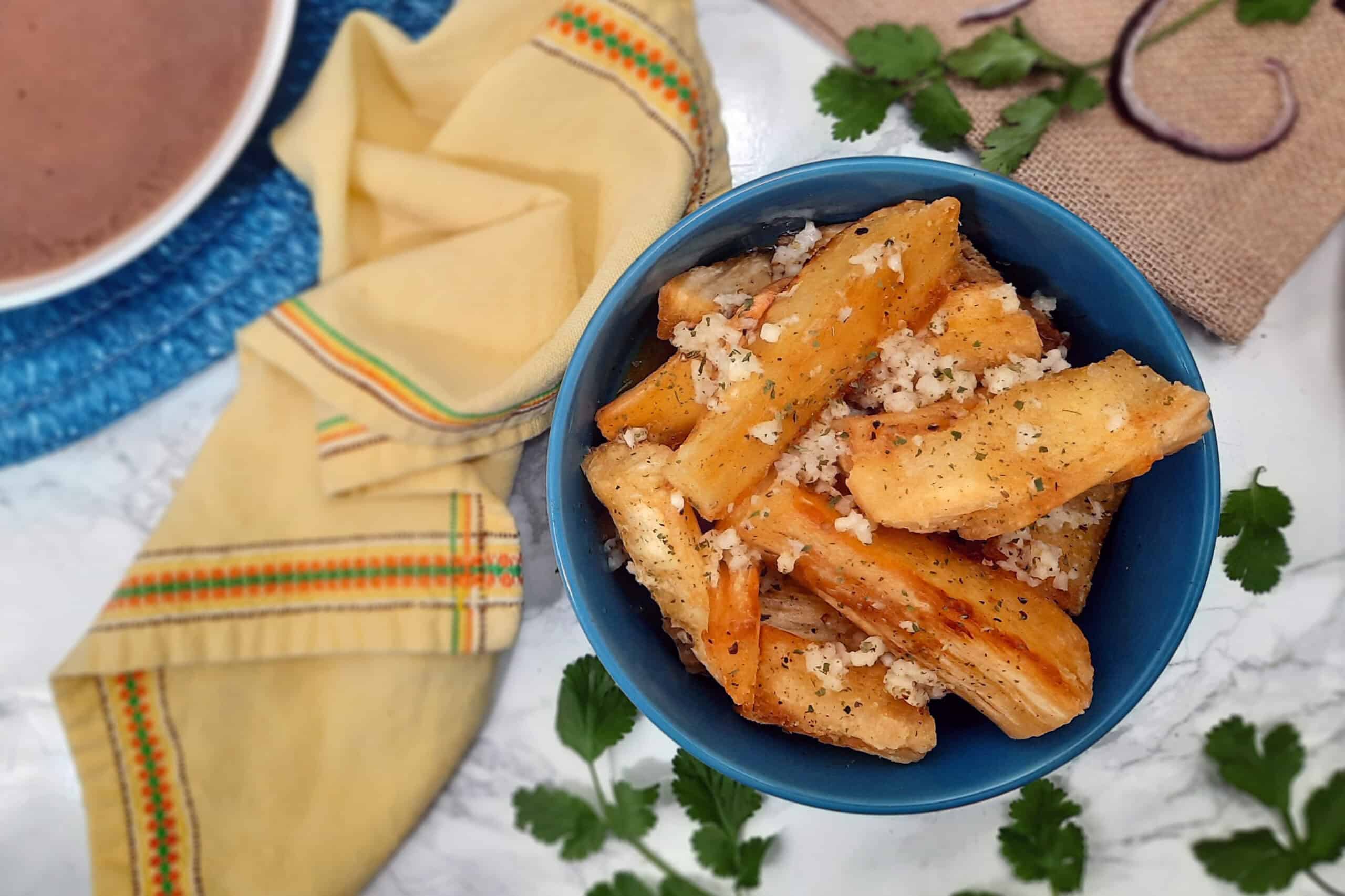 Yuca-frita-con-mojo-offcenter-in-blue-bowl-with-yellow-napkin-and-garnish