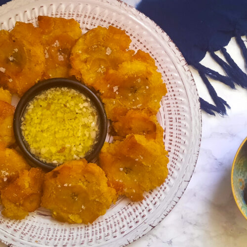 top-view-fried-green-plantains-Cuban-Tostones-con-mojo-on-round-plate