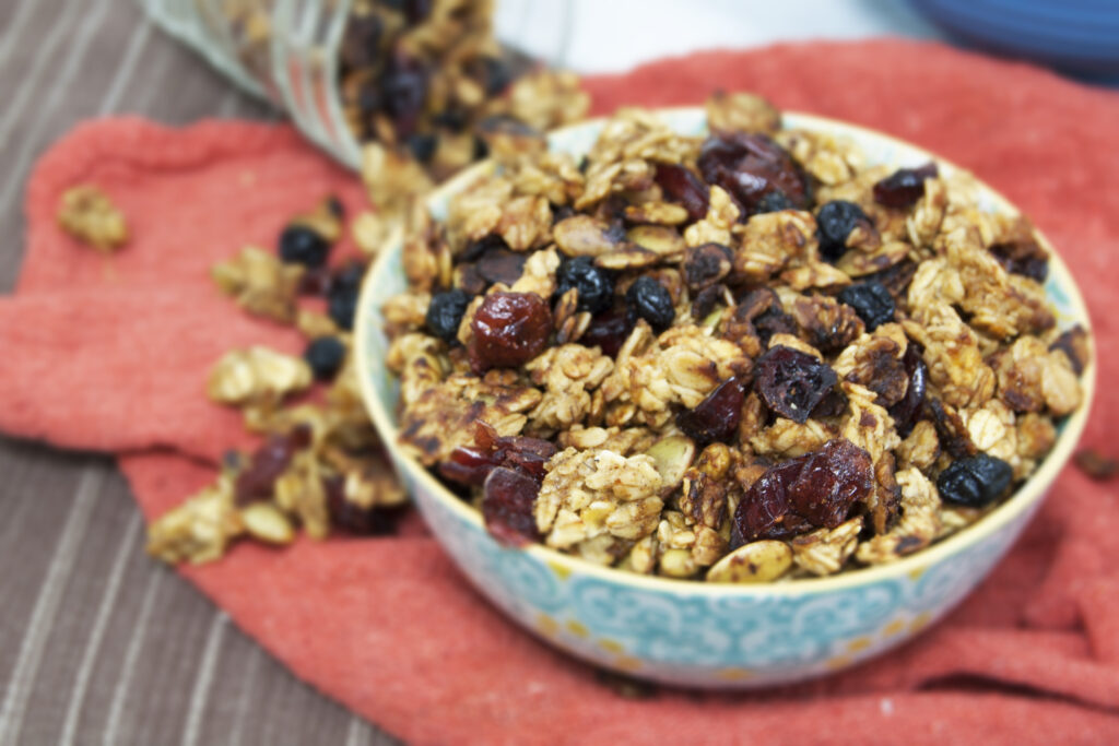 filled-bowl-of-allergy-free-carmelized-banana-orange-chai-granola-with-spilling-jar-in-background