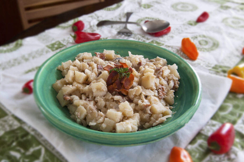 Kartoffelsalat-German-potato-salad-garnished-with-bacon-in-round-green-bowl-surrounded-by-sweet-peppers