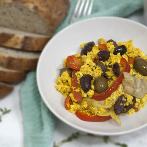 mediterranean-tofu-scramble-in-round-white-bowl-served-with-olives-peppers-and-artichokes