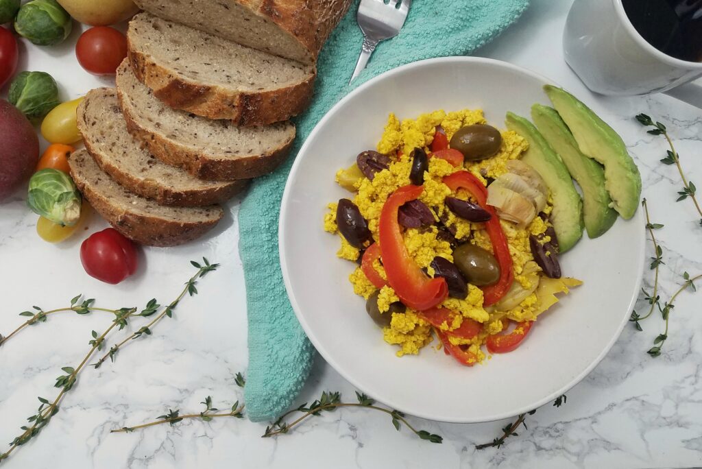 white-bowl-of-mediterranean-tofu-scramble-with-olives-peppers-and-artichokes-served-with-bread