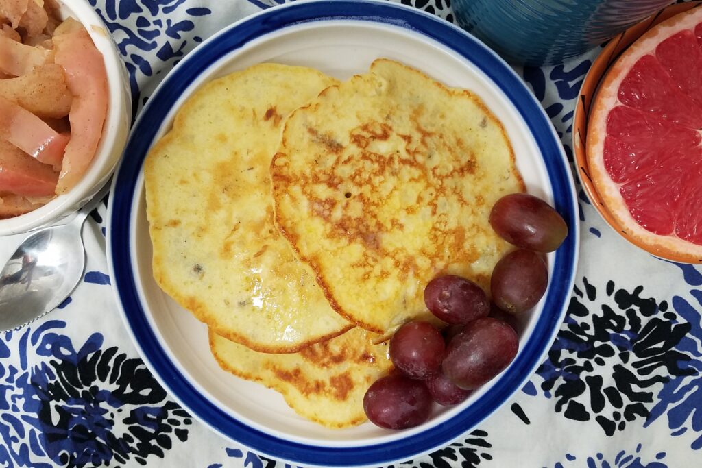 top-view-three-potato-pancakes-on-blue-and-white-plate-served-with-grapes