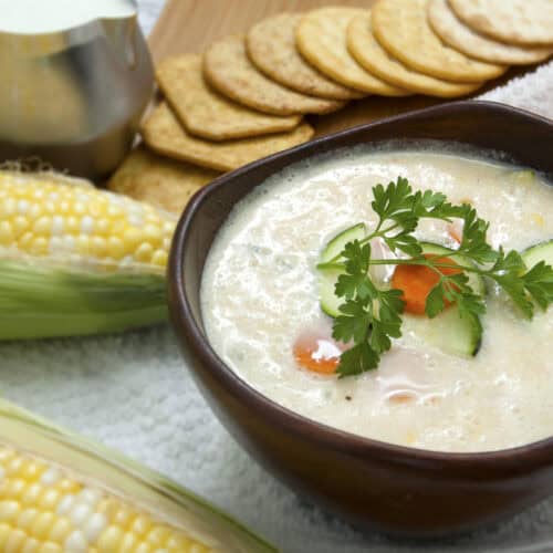 sweet-corn-zucchini-soup-in-brown-wooden-bowl-with-crackers-and-parsley