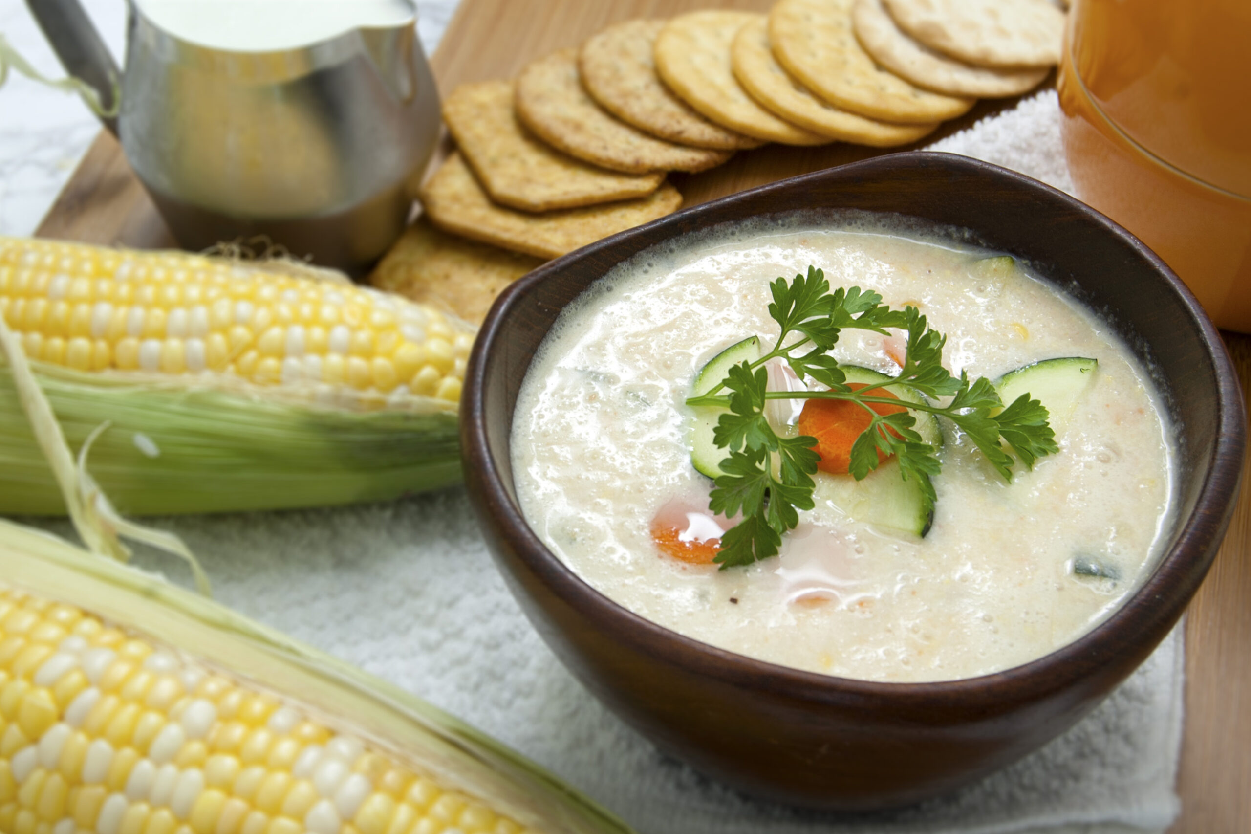 sweet-corn-zucchini-soup-in-brown-wooden-bowl-with-crackers-and-parsley