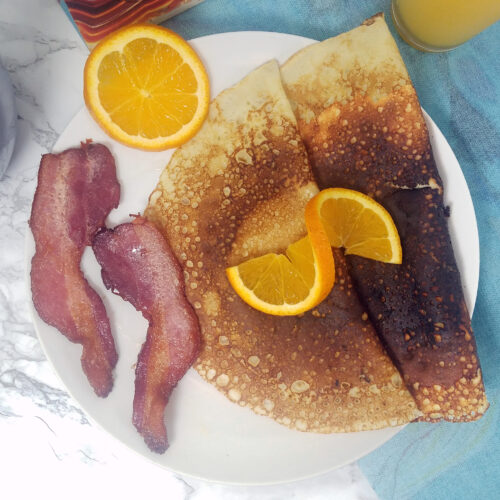 two-folded-breakfast-Swedish-pancakes-with-two-slices-bacon-garnished-with-orange-slice