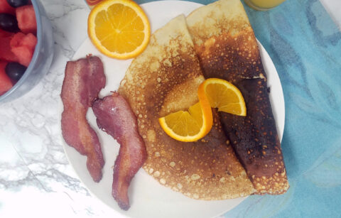 two-folded-breakfast-Swedish-pancakes-with-two-slices-bacon-garnished-with-orange-slice