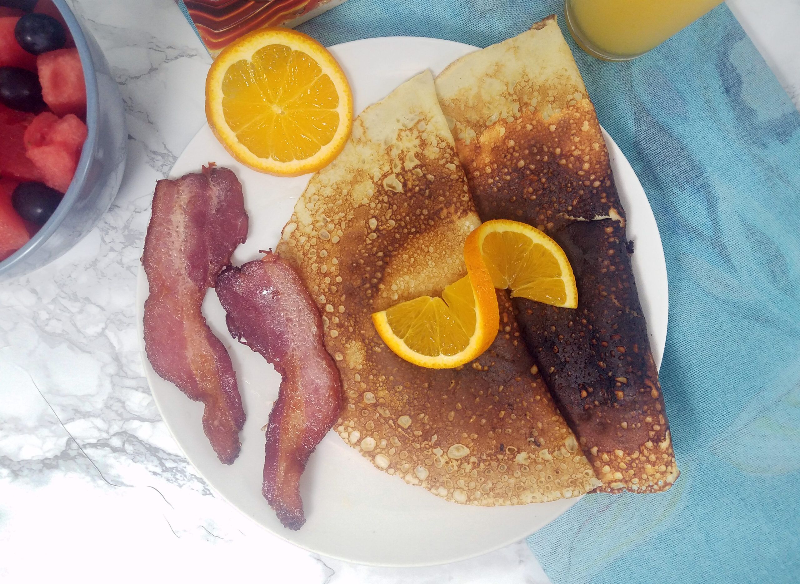 two-folded-breakfast-Swedish-pancakes-with-two-slices-bacon-garnished-with-orange-slice