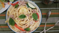 top-view-white-sauce-fettuccine-with-sausage-and-vegetables-on-green-striped-background