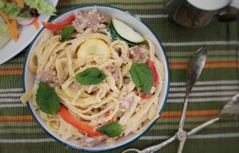 top-view-white-sauce-fettuccine-with-sausage-and-vegetables-on-green-striped-background