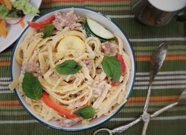 top-view-white-sauce-fettuccine-with-sausage-and-vegetables-on-green-striped-background