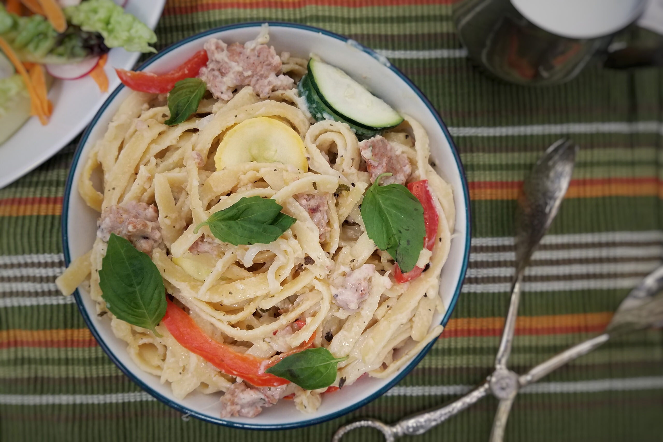 top-view-white-sauce-fettuccine-with-sausage-and-vegetables-on-green-striped-background