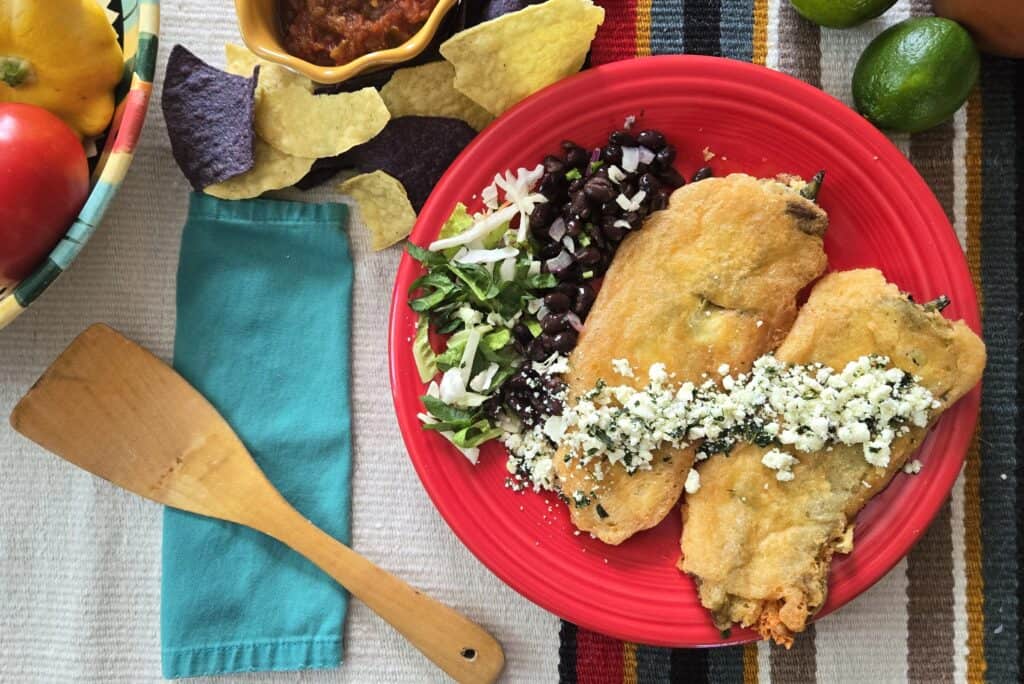 two-battered-chiles-rellenos-made-with-Hatch-peppers-garnished-with-cotija-on-red-plate