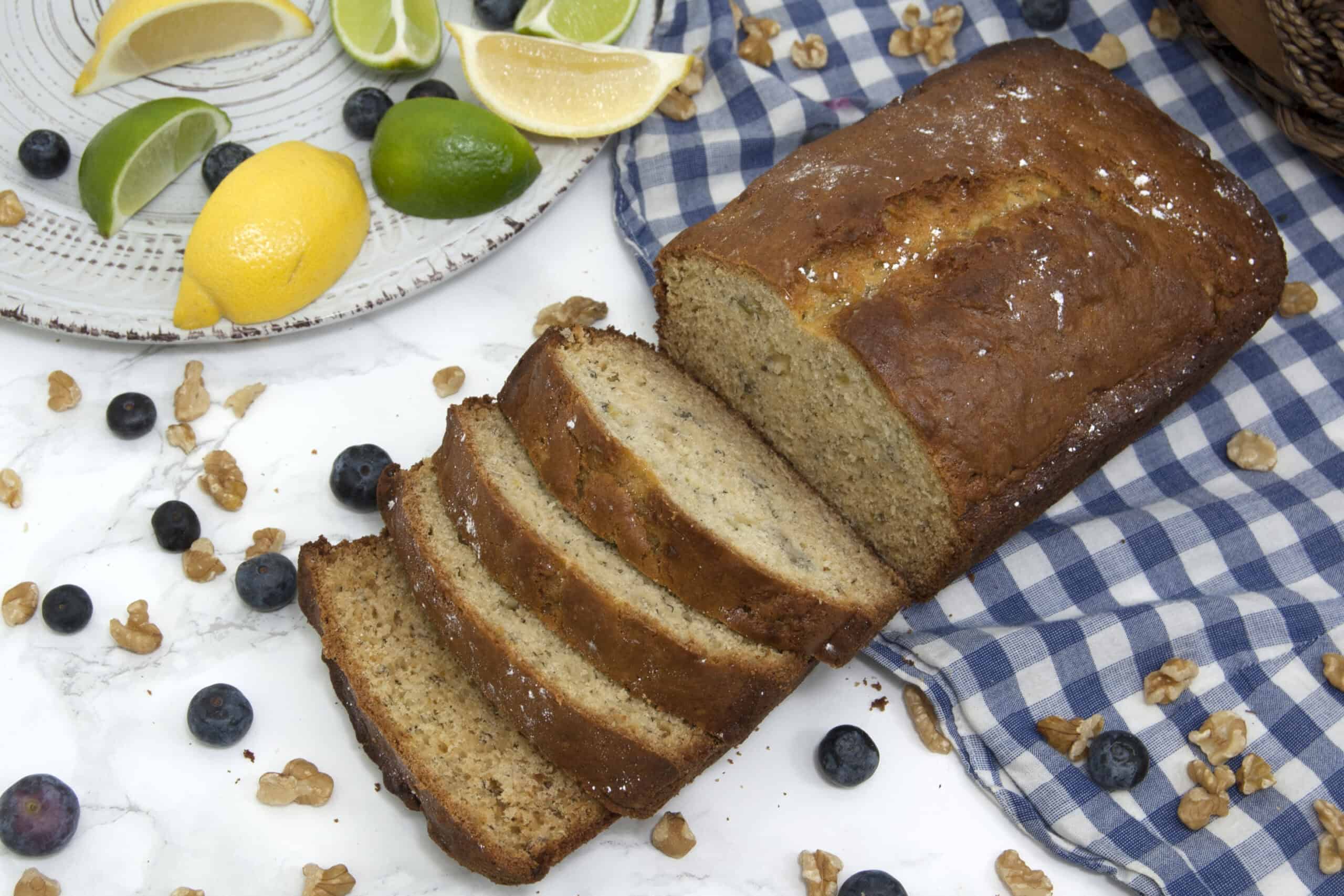 loaf-of-sliced-banana-bread-garnished-with-blueberries-powdered-sugar-walnuts-and-citrus-on-checkered-tablecloth