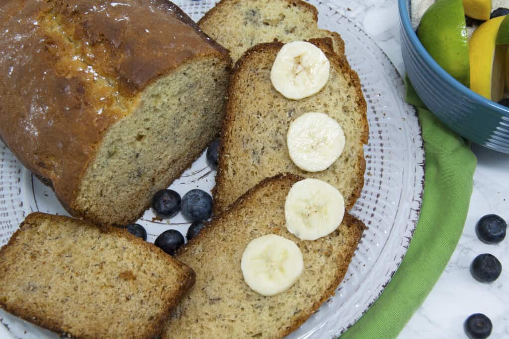 sliced-banana-bread-and-loaf-on-white-plate-garnished-with-bananas