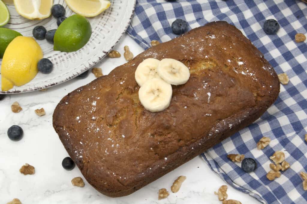 unsliced-loaf-of-moms-banana-bread-garnished-with-powdered-sugar-and-sliced-bananas