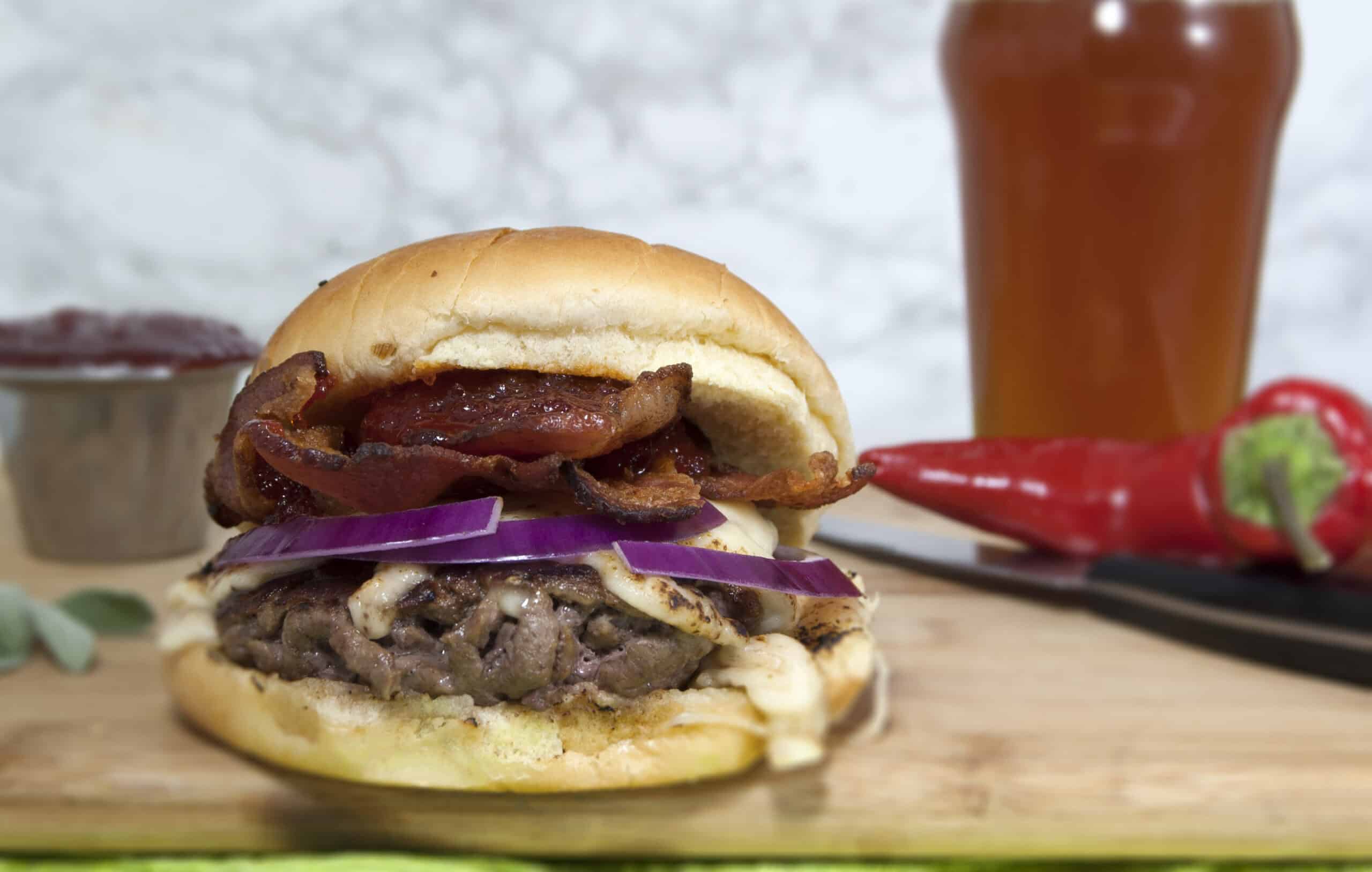 smash-burger-with-Havarti-red-onions-and-red-pepper-jelly-served-on-cutting-board-with-beer